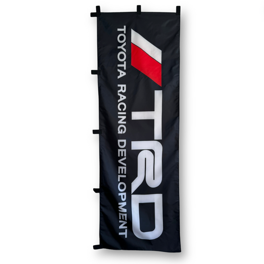 A rectangular flag with the TRD text in white on a black background and Toyota Racing Development text in white below.
